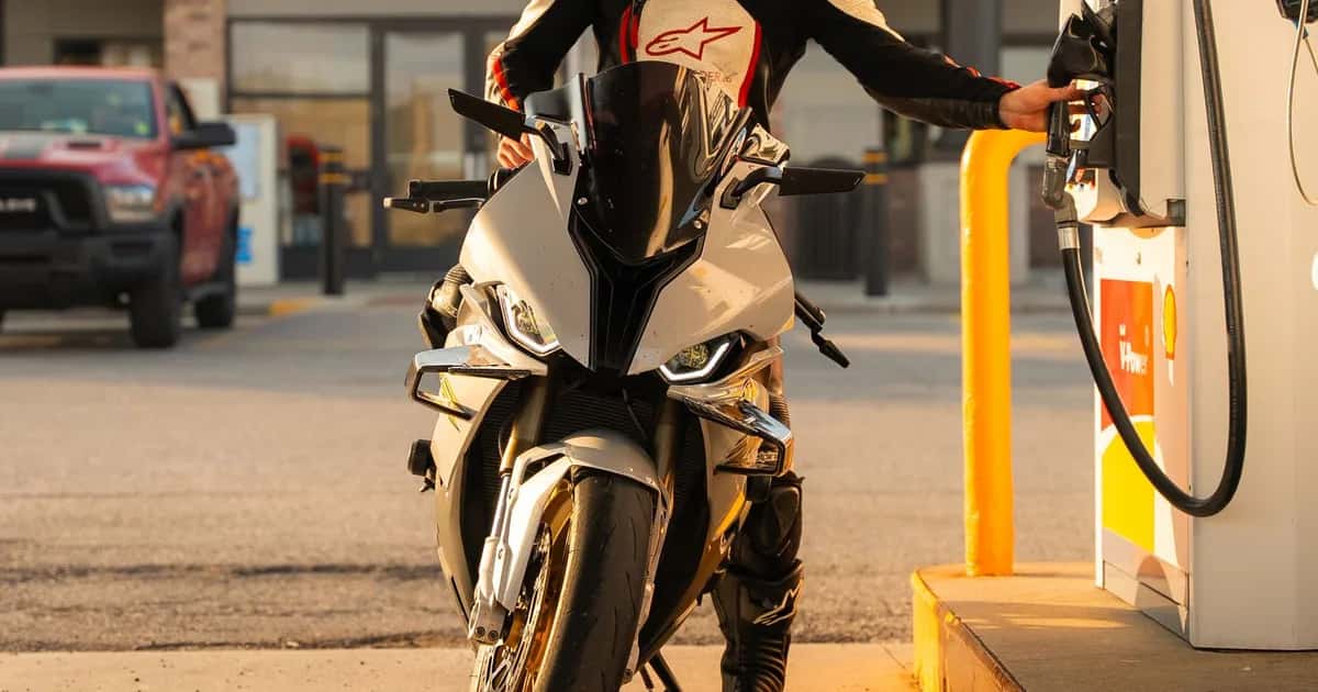 Motociclista abastece a moto na bomba de um posto, com a mão no bico de combustível