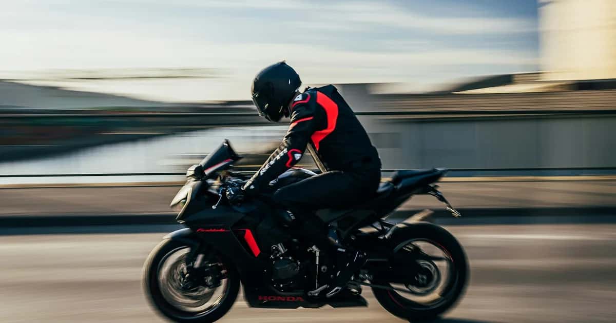 Motociclista com capacete integral, jaqueta com protetores e luvas pilota em via urbana, em foto com fundo em movimento