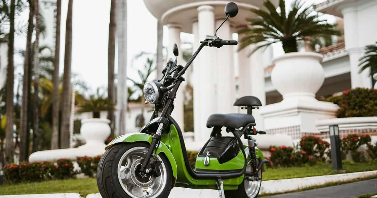 Scooter elétrica verde de pneus largos estacionada em área externa, sem placa