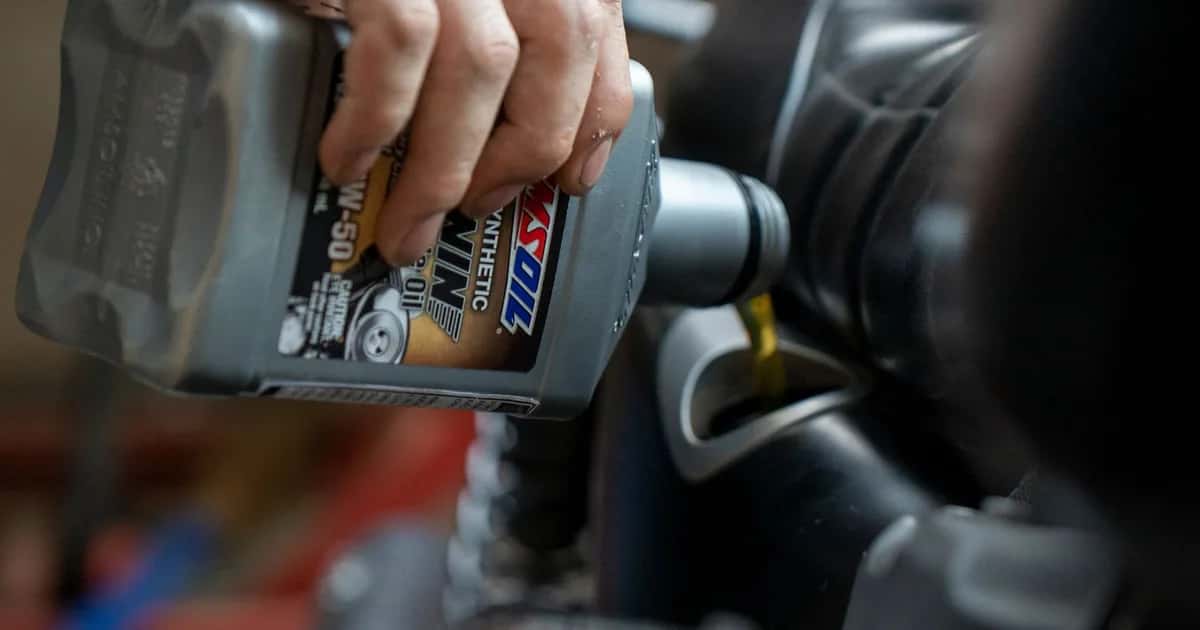 Mão verte óleo dourado do frasco direto no bocal do motor de uma moto, em close de garagem