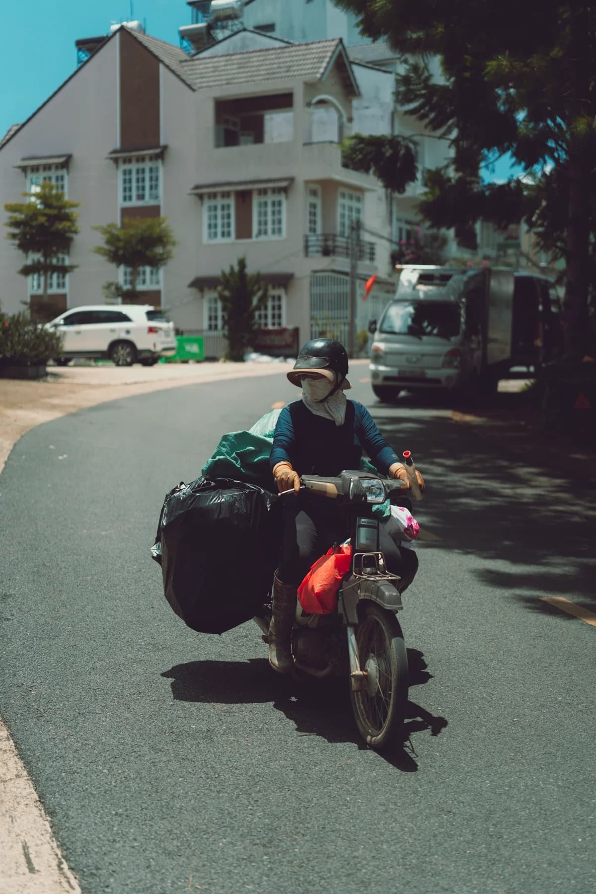 Motociclista com carga rodando em rua de cidade em dia de sol