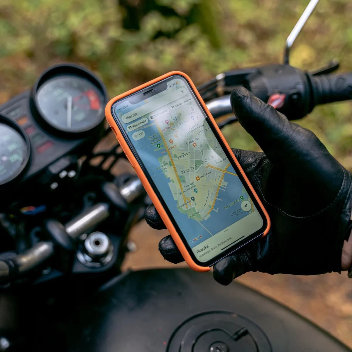 Mão enluvada segura smartphone com aplicativo aberto, painel de moto ao fundo