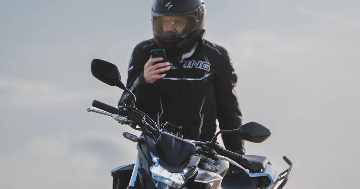 Motociclista de capacete consulta o celular montado na moto, em ambiente aberto