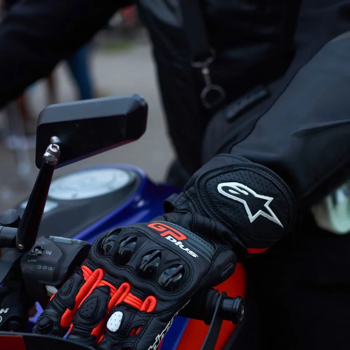 Mão com luva de proteção com casca rígida apoiada no comando da moto, em close