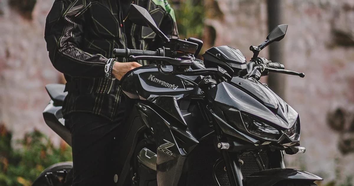Motociclista de jaqueta preta de couro sentado em moto esportiva em piso de pedra sob sol forte