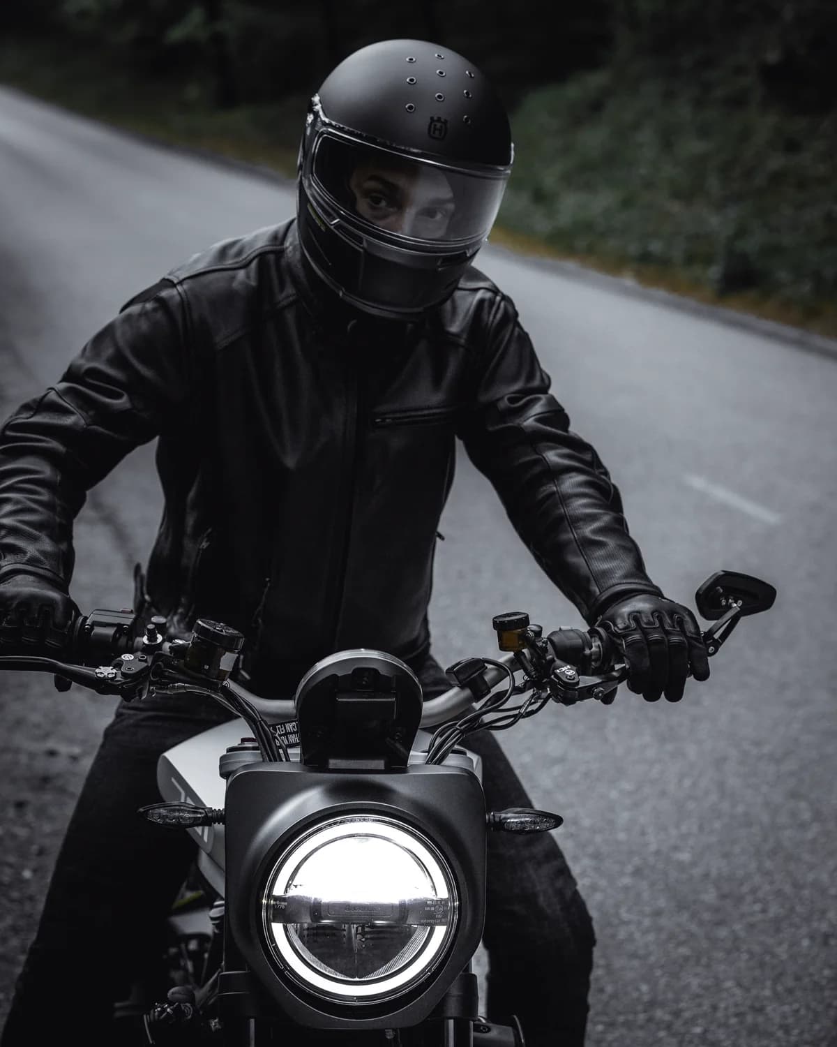 Motociclista de jaqueta preta em estrada de terra entre árvores