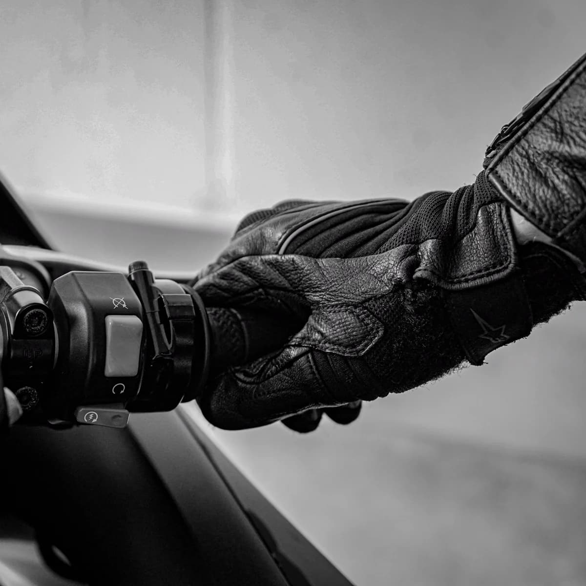 Mão com luva segurando guidão de moto em preto e branco
