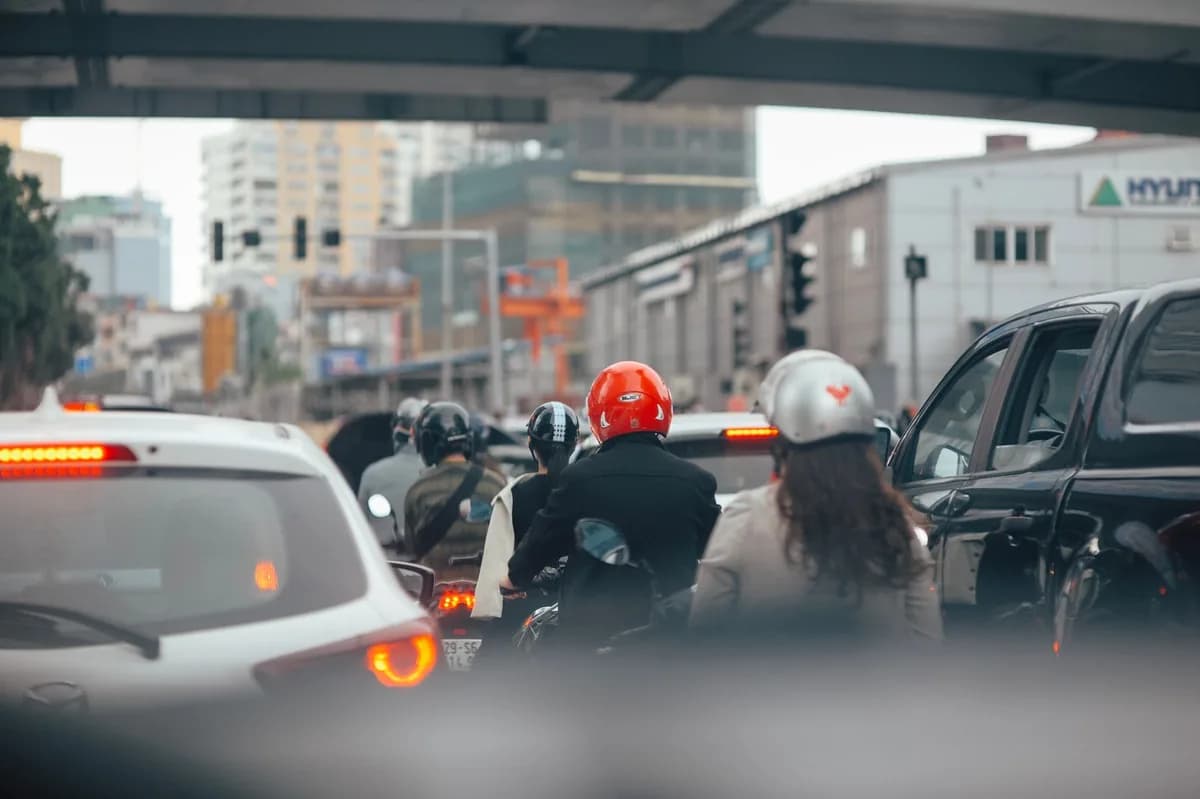 Motociclistas avançam entre carros parados em avenida movimentada, sob um viaduto