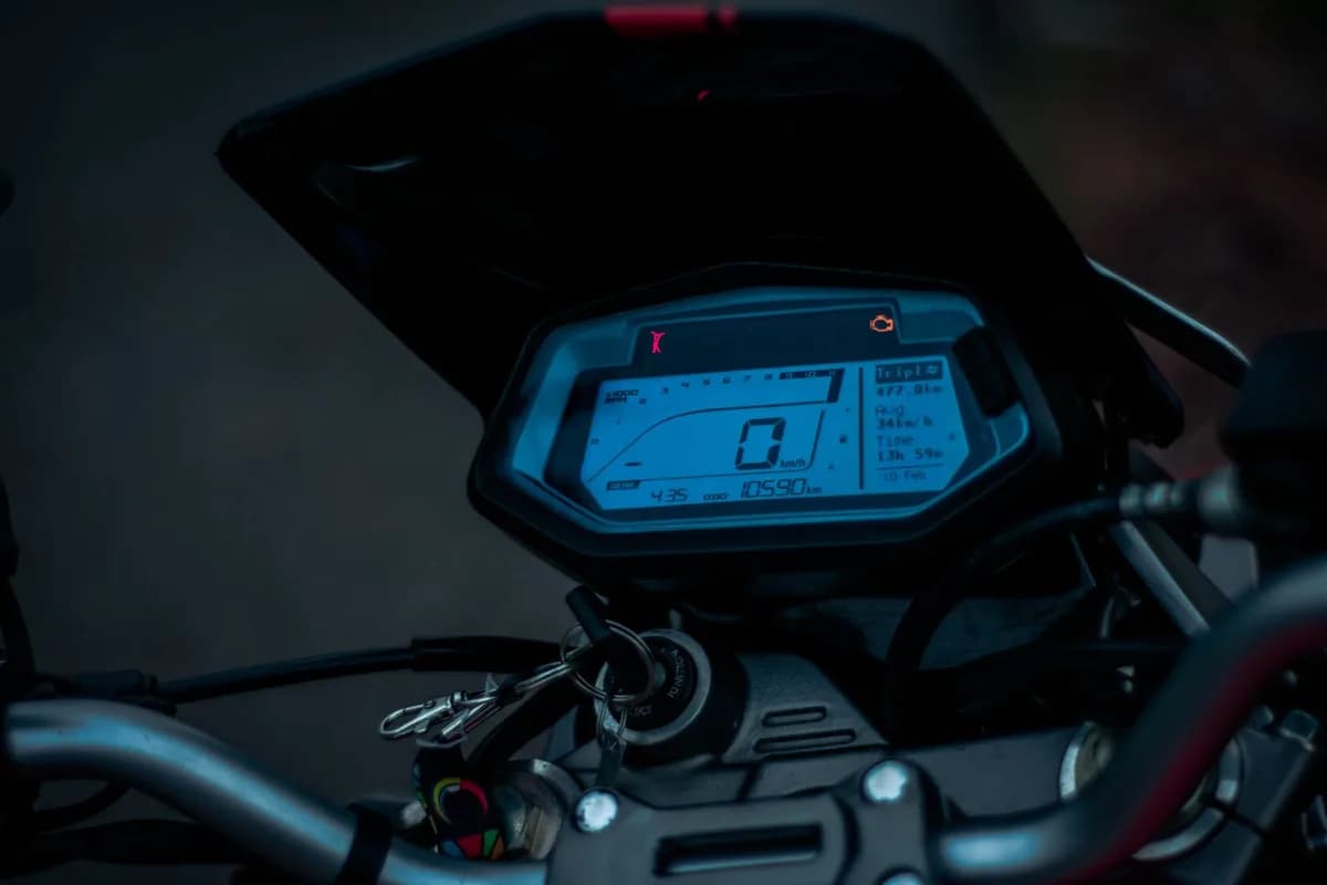 Painel digital de moto em close, com velocímetro zerado e hodômetro marcando 10.590 km