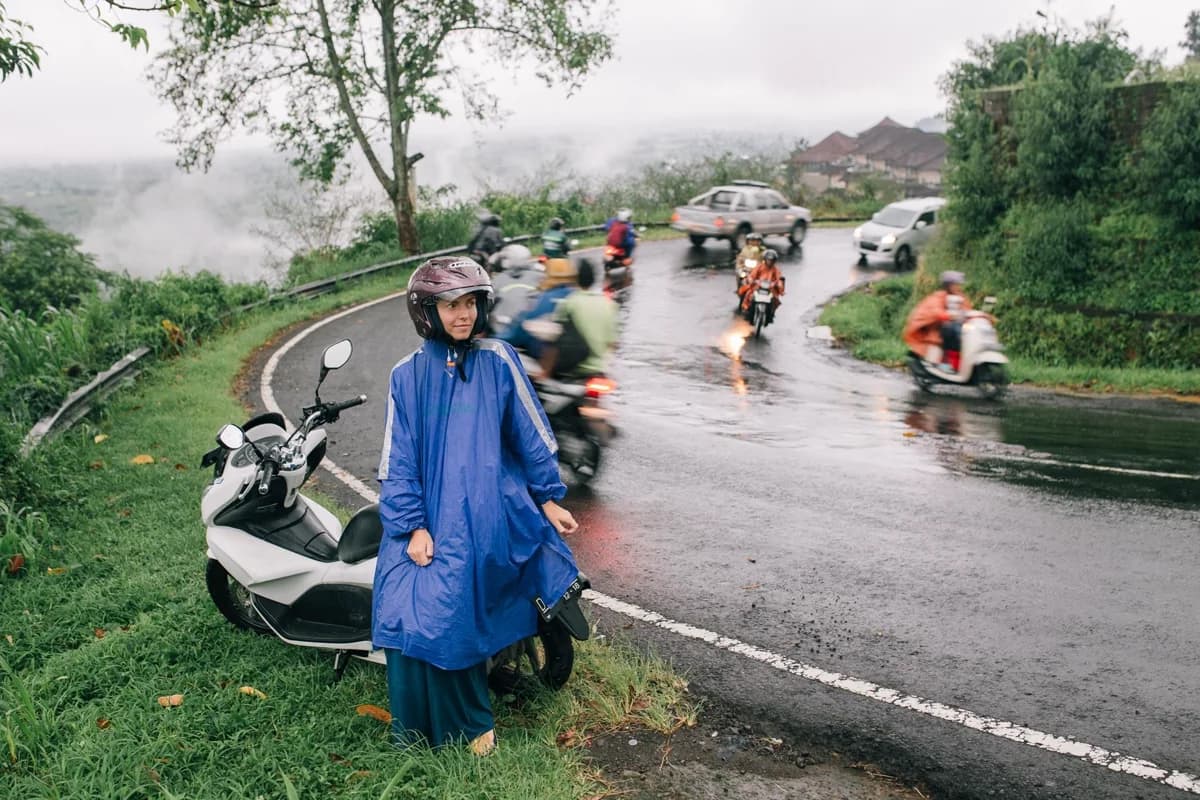 Mulher de capa de chuva sentada em moto parada no acostamento