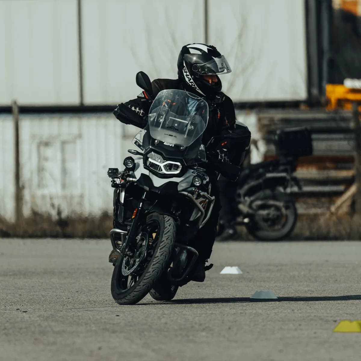 Piloto de capacete e equipamento treina manobras em moto de baixa cilindrada em área aberta pavimentada