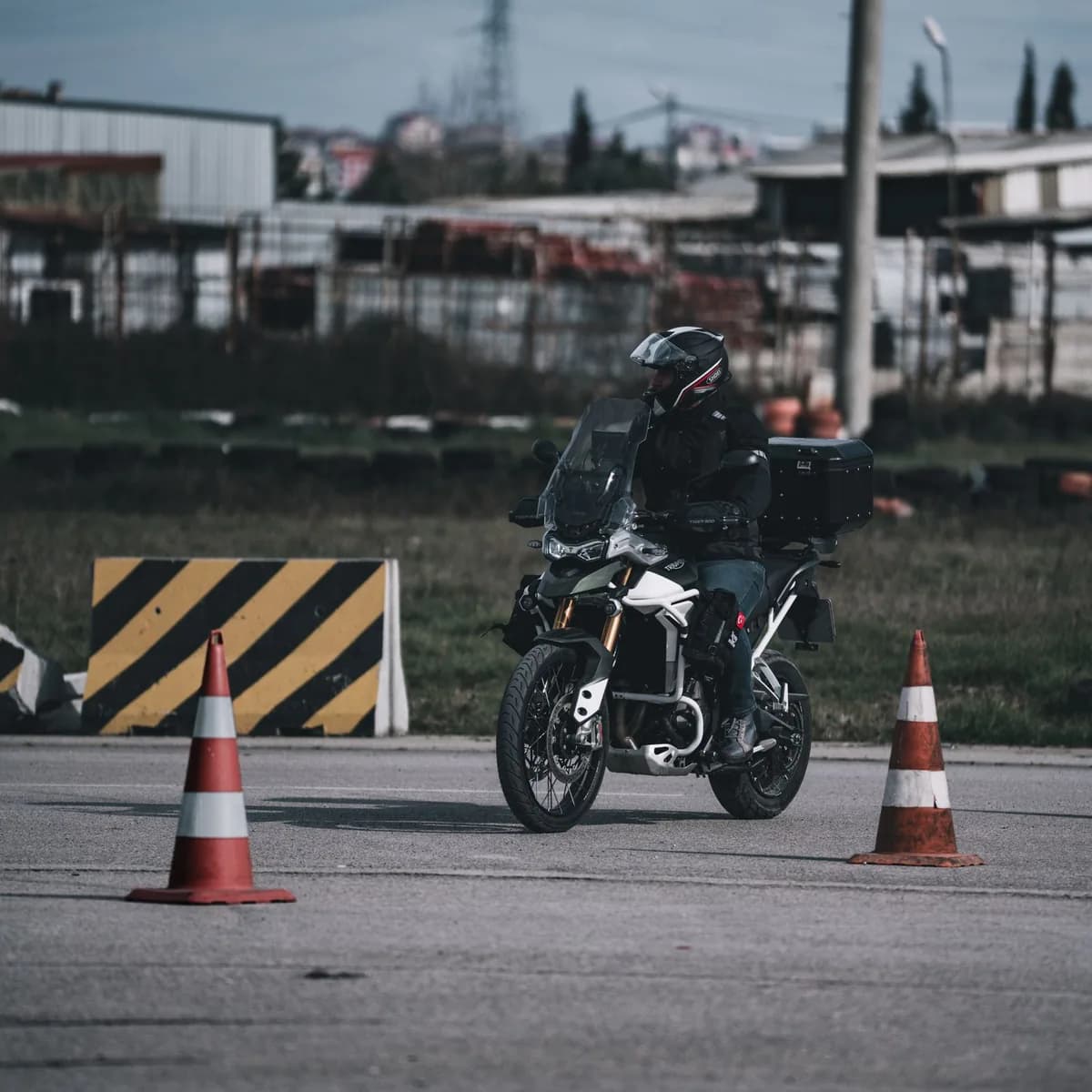 Motociclista de capacete contorna cones laranja em percurso de treino de manobra ao sol