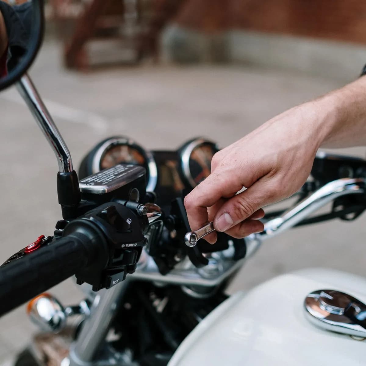 Mão aperta uma chave fixa junto ao guidão de uma moto, em close ao ar livre