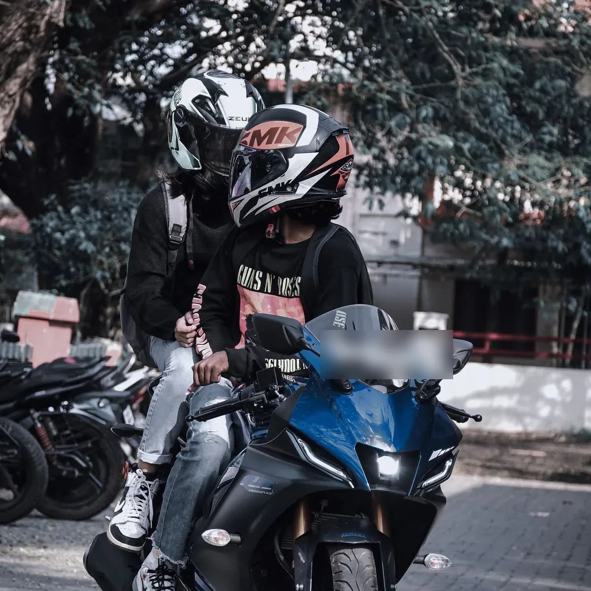 Condutor e passageiro, cada um com o próprio capacete de viseira, na mesma moto em rua arborizada