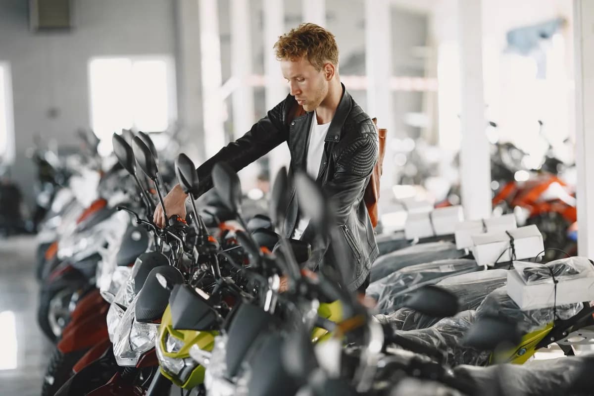 Cliente examina fileira de motos de baixa cilindrada novas em pátio de concessionária com luz natural