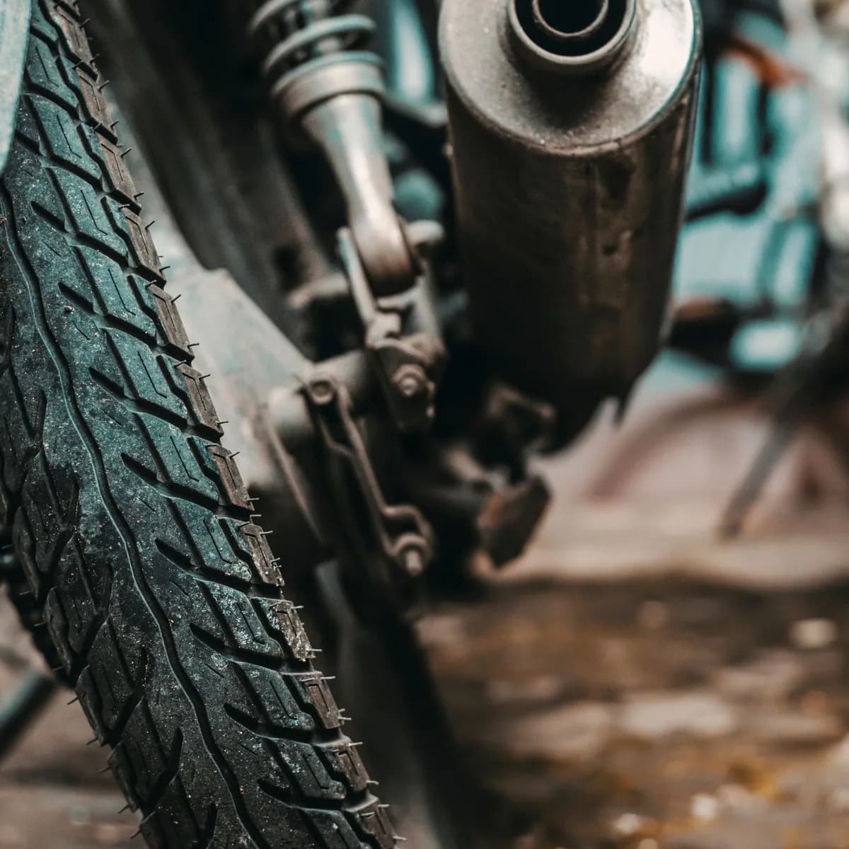 Close do escapamento e do pneu traseiro de uma moto de uso diário, com desgaste visível