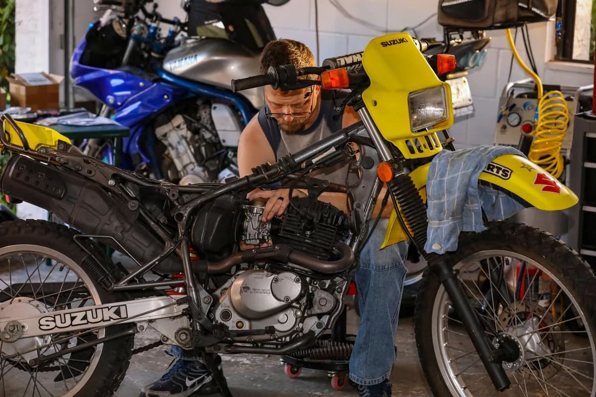 Mecânico debruçado sobre o motor de uma moto em oficina de verdade, com ferramentas e peças em volta