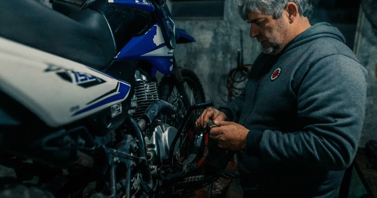 Homem reparando moto em garagem escura com perícia mecânica